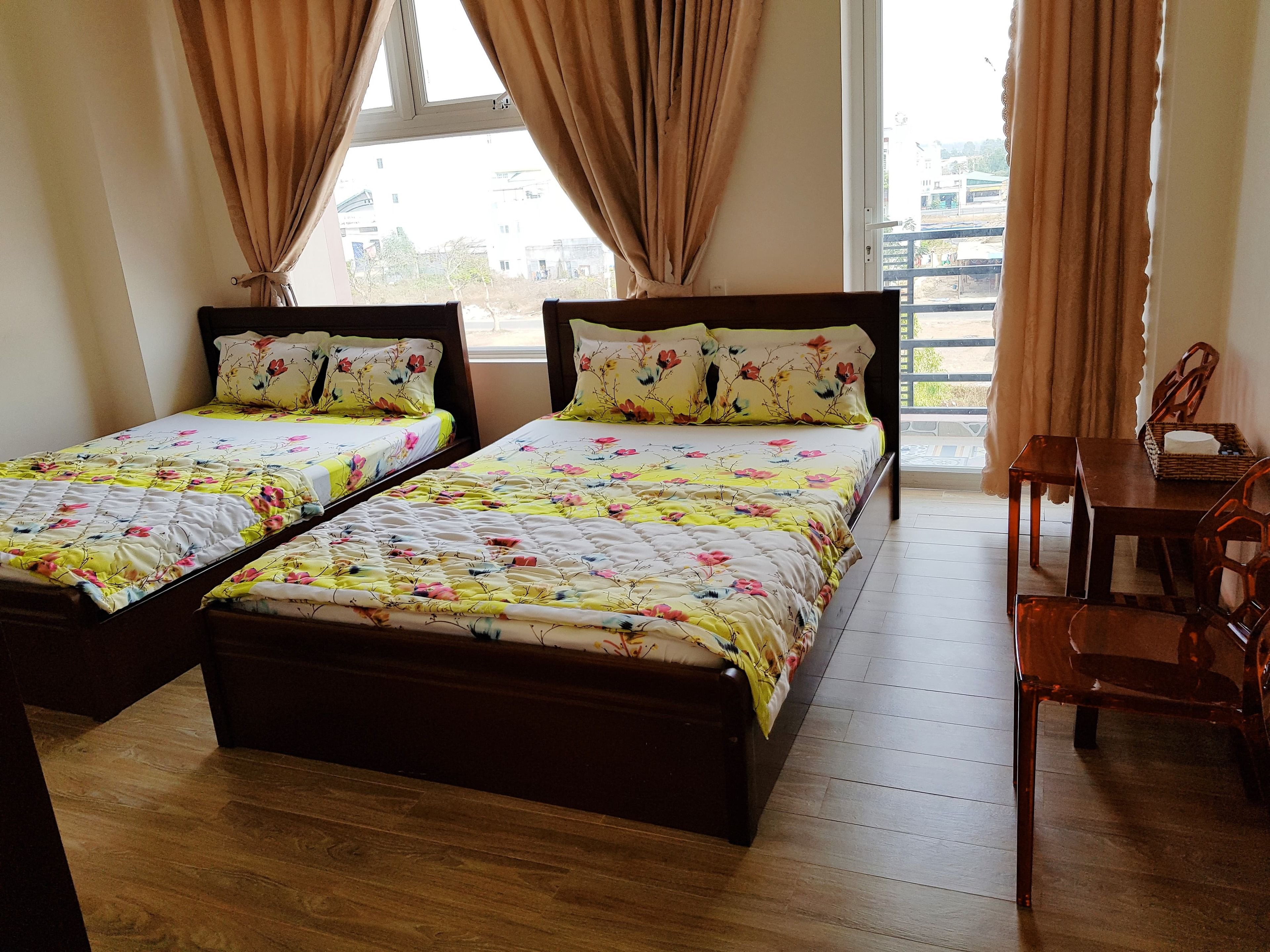 Una habitación con dos camas de madera, cada una con ropa de cama floral, una mesa de madera con sillas y una ventana con cortinas.