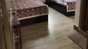 Una habitació amb dos llits, una taula petita i una finestra amb un disseny de celosies.