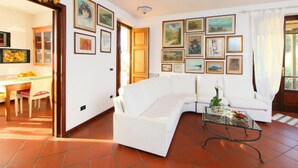 Una sala de estar con un sofá blanco, una mesa de centro de vidrio y un comedor con una mesa y sillas de madera.