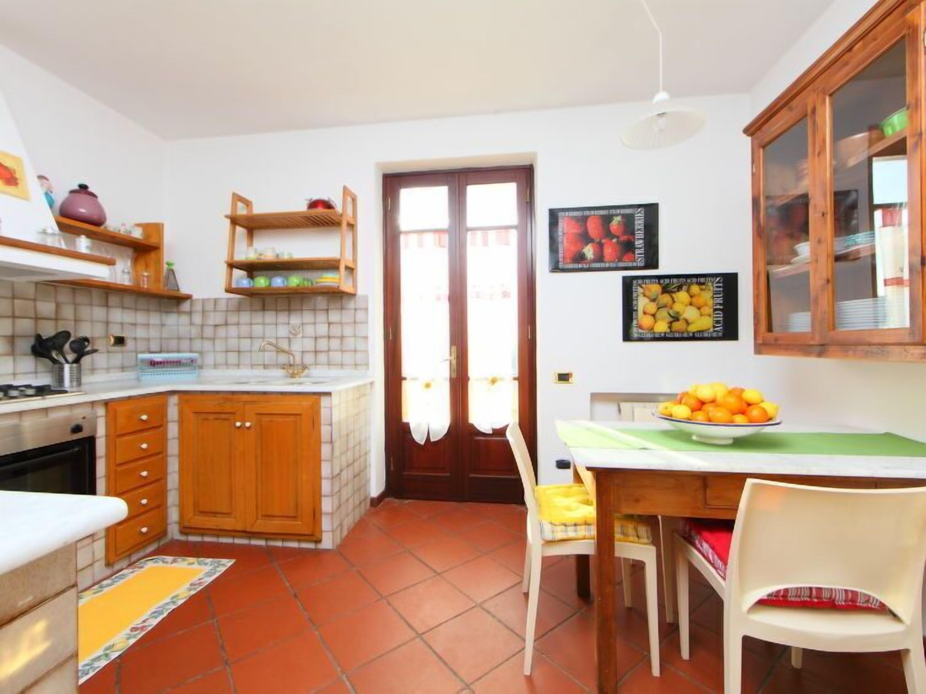 A compact kitchen with wooden cabinets, a tiled backsplash, a dining table with chairs, and a fruit bowl.