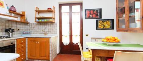 A compact kitchen with wooden cabinets, a tiled backsplash, a dining table with chairs, and a fruit bowl.
