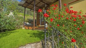 Una casa de madera con techo de paja, rodeada de un jardín bien cuidado con flores rojas y césped verde.