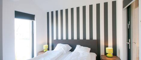 A modern bedroom with a large bed, striped wall, and two bedside tables with lamps.