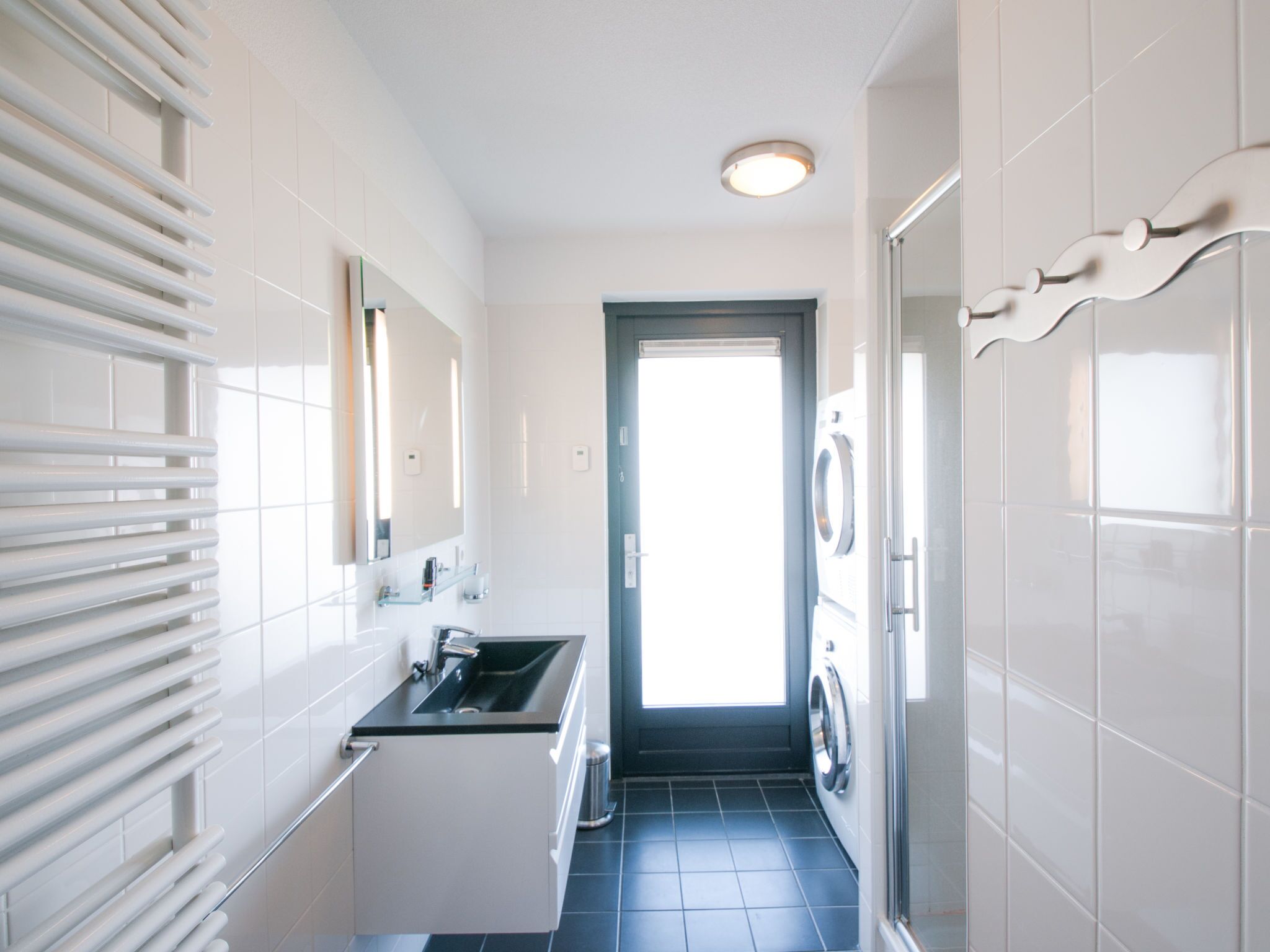 A modern bathroom with a sink, mirror, and a door leading to a laundry area.