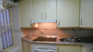 Een kleine keuken met een spoelbak, fornuis en oven.