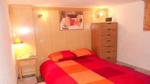 Een slaapkamer met een bed, nachtkastje, dressoir en een wandlamp.
