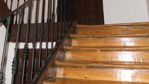 Een houten trap met zwarte spijbels die leidt naar een donker houten deur met een messing knop.