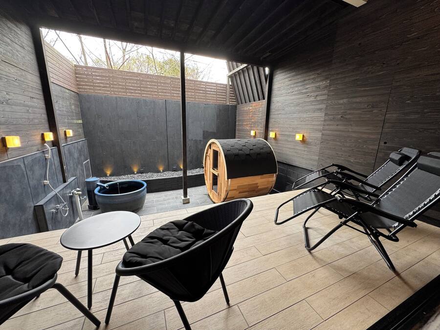 Ett modernt utomhusområde för avkoppling med en trähusad bastu, ett massagebord och en sittgrupp med stolar och ett bord.