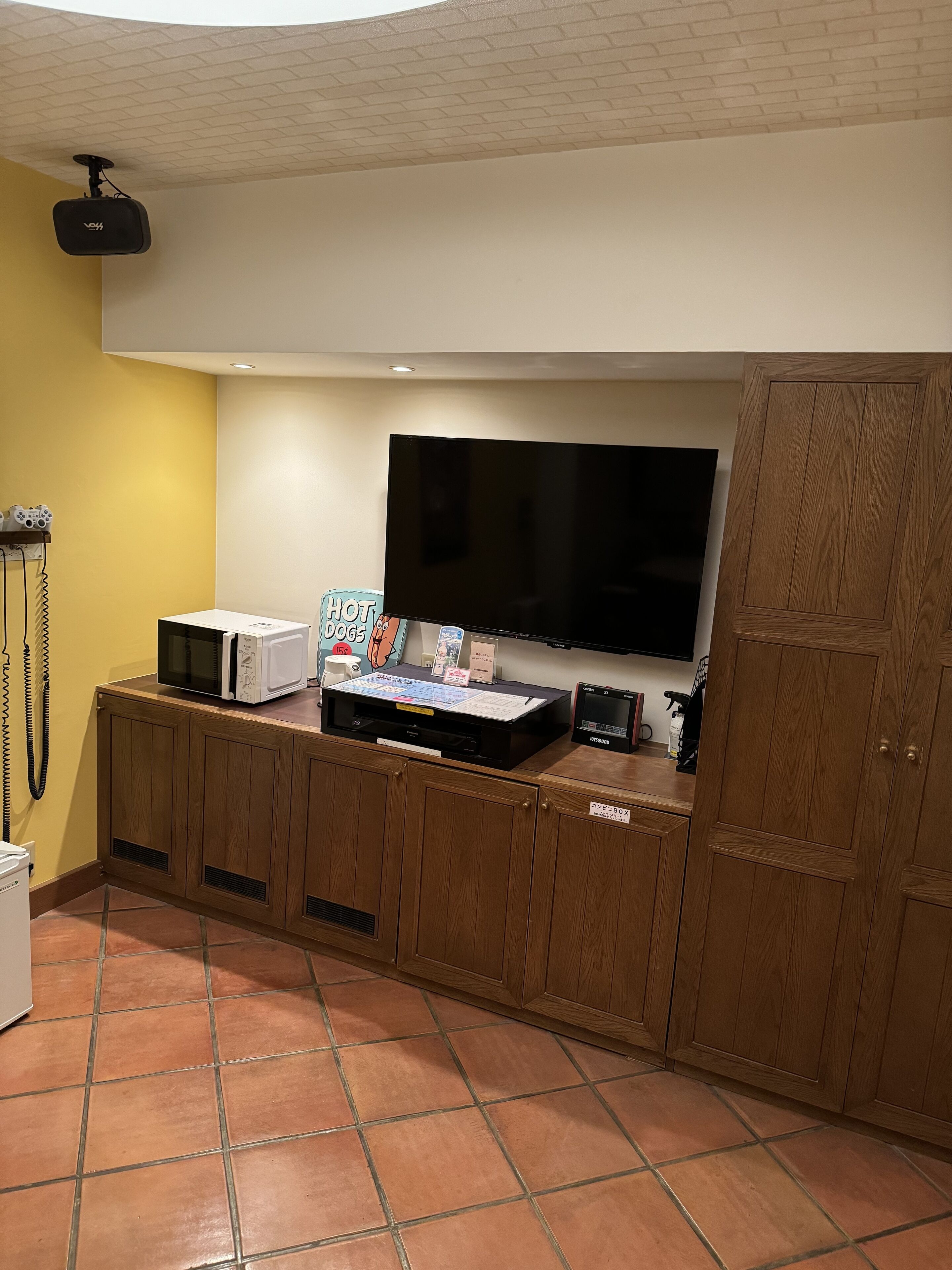 Ein Zimmer mit einem an der Wand befestigten Flachbildfernseher, einer Mikrowelle und einem kleinen Schrank mit einem Schild.
