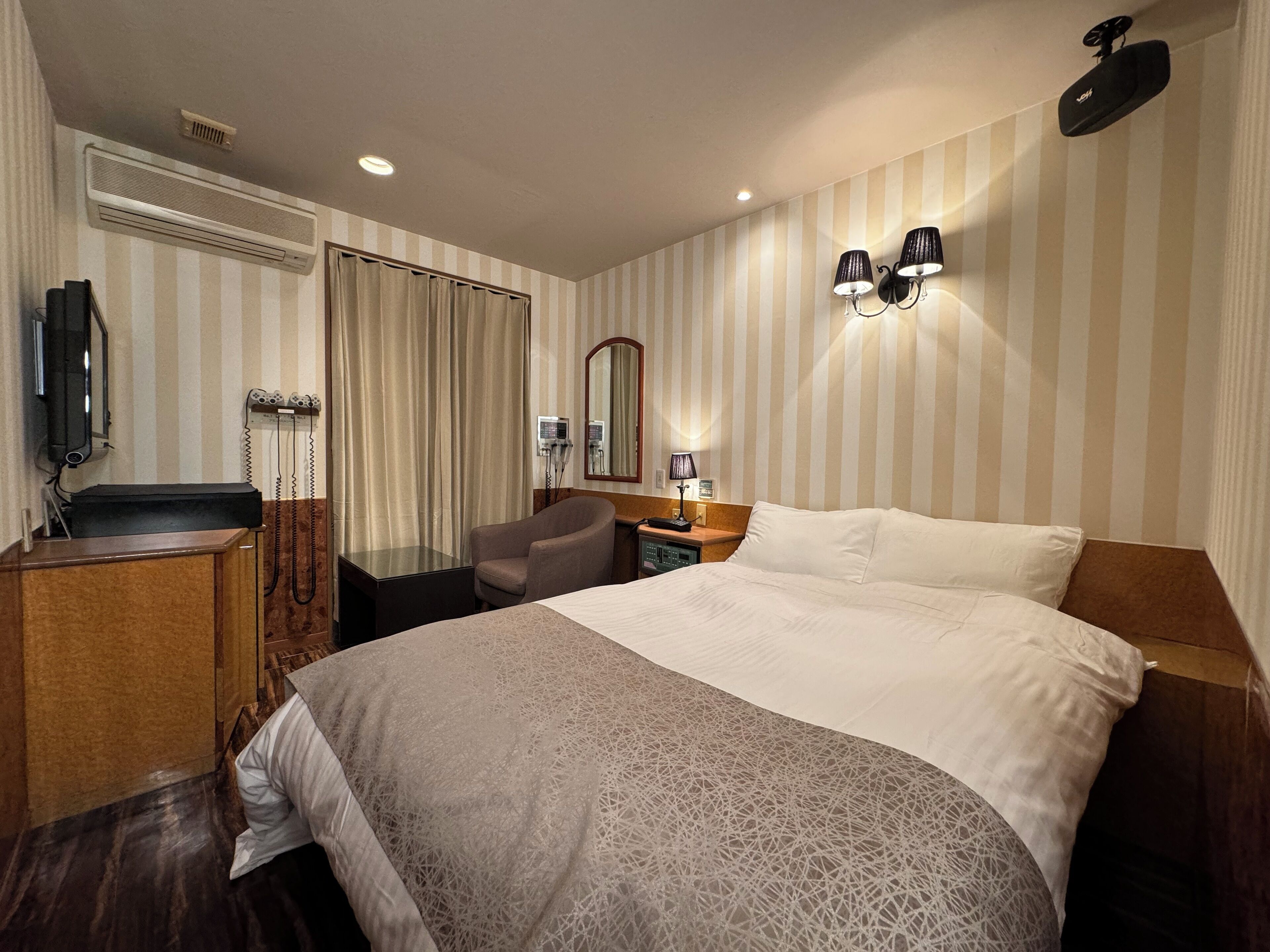 Ein Hotelzimmer mit einem Bett, einem Schreibtisch mit Stuhl, einem Fernseher, einem Spiegel und einer Wandleuchte.