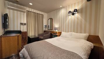 Ein Hotelzimmer mit einem Bett, einem Schreibtisch mit Stuhl, einem Fernseher, einem Spiegel und einer Wandleuchte.
