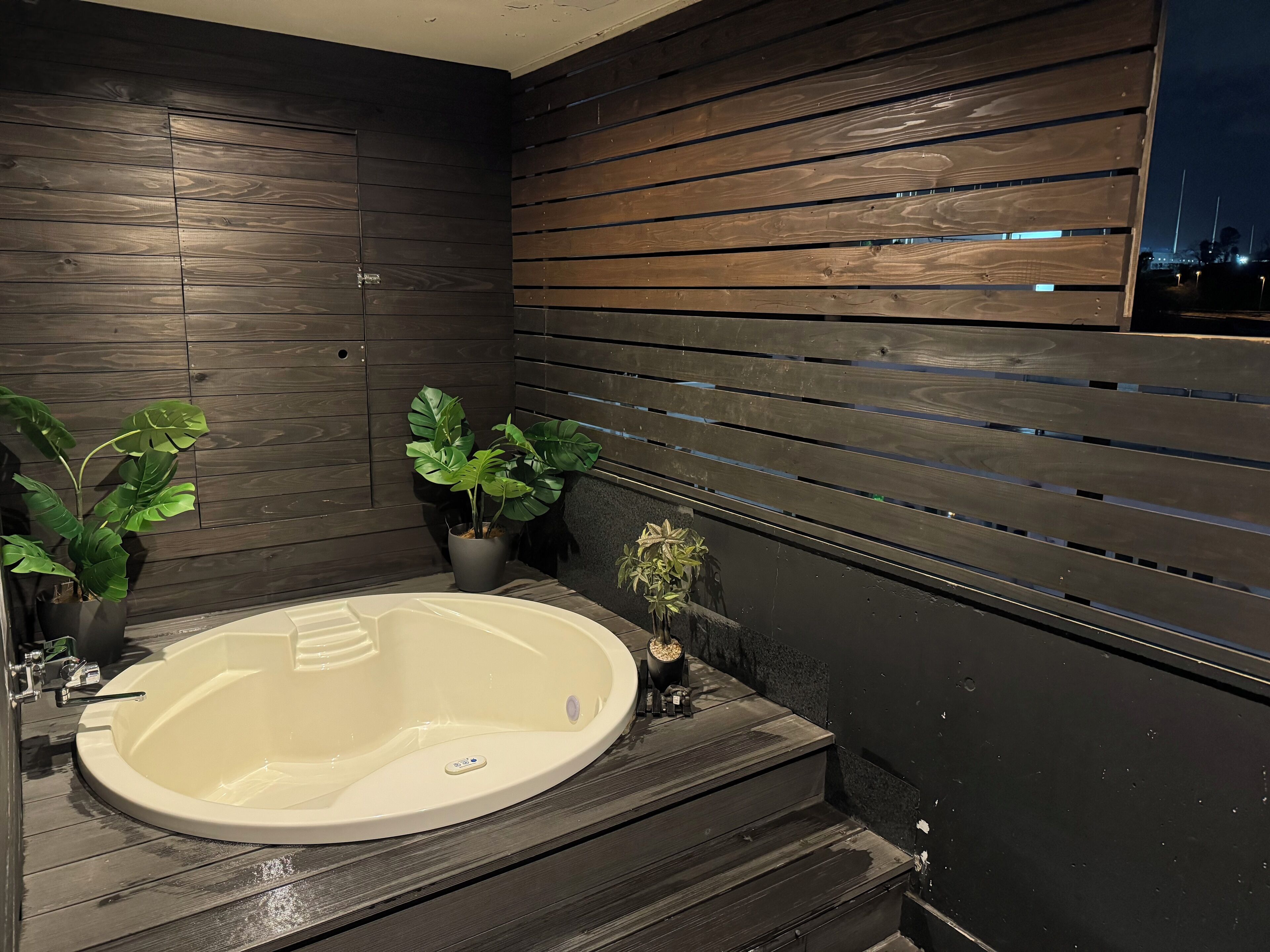A modern bathroom with a freestanding bathtub, dark wooden walls, and potted plants.