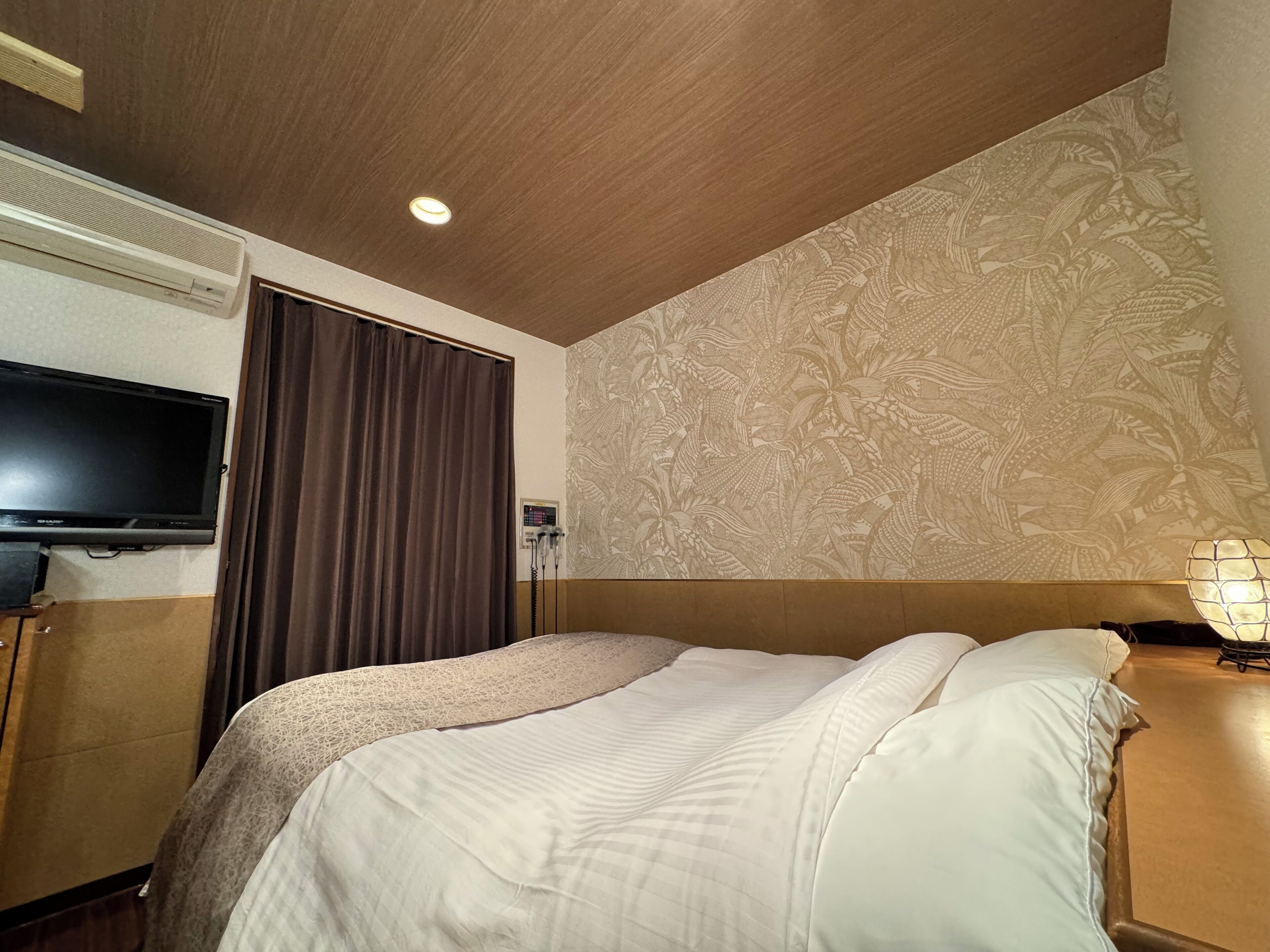 Una camera d'albergo con un letto, una televisione, una parete decorata con un motivo floreale e una lampada a soffitto.