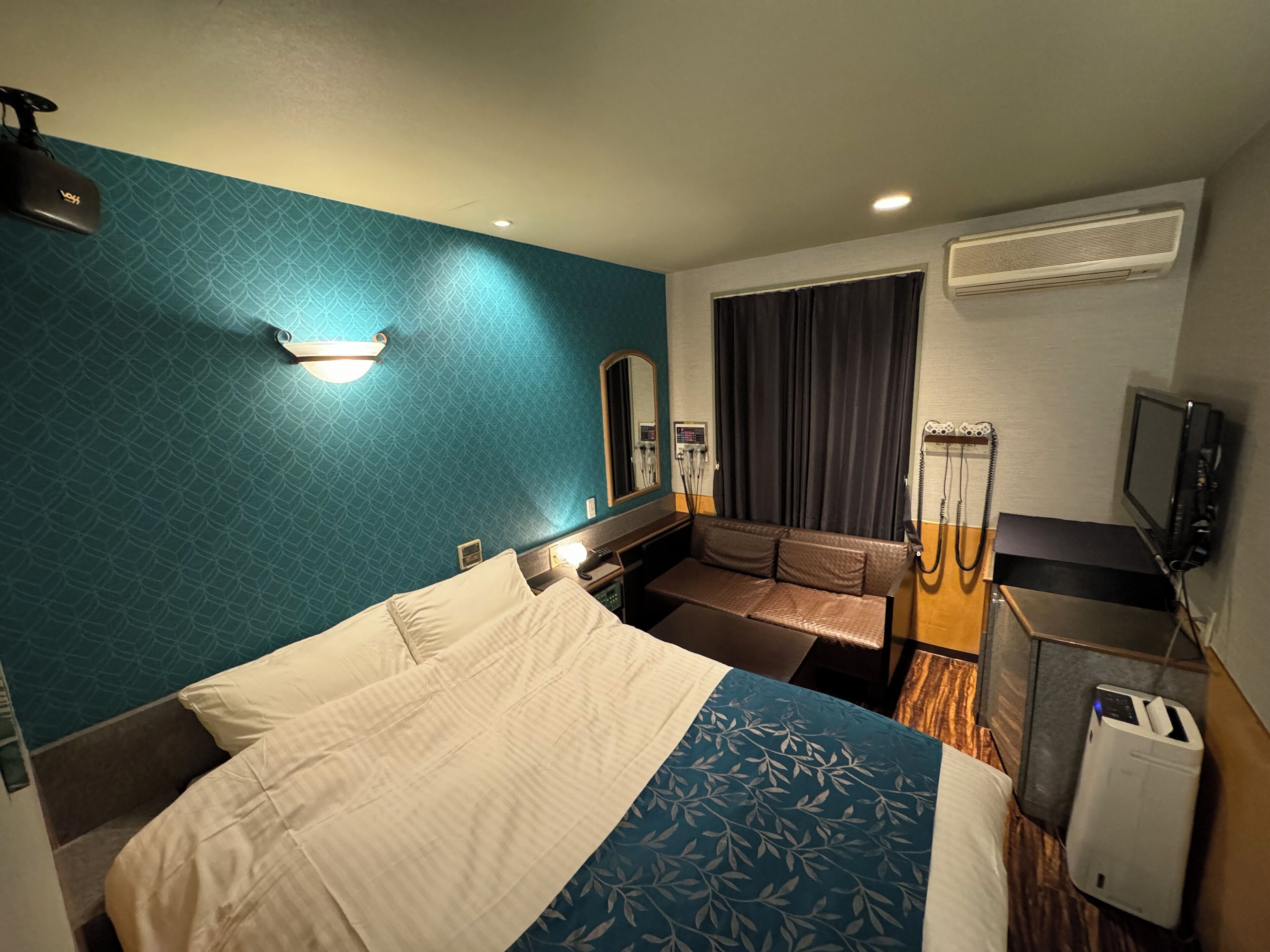 A hotel room with a bed, a seating area, a TV, and an air conditioning unit.