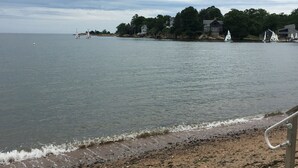 A beach with a calm sea, a few sailboats, and houses along the shore.