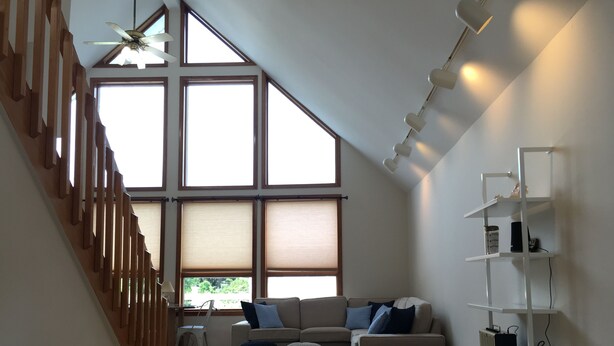 A spacious loft bedroom with a large window, a wooden staircase, a sofa, ottomans, and a white shelving unit.