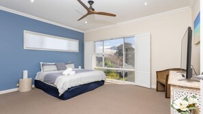 Ein Schlafzimmer mit einem Bett, einem Deckenventilator, einem großen Fenster und einem Fernseher.