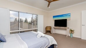 A hotel room with a bed, a television on a wooden stand, a chair, and a painting of a beach scene.