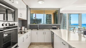 A modern kitchen with a large island, built-in appliances, and a view of the city skyline. - Sun City Ocean Views (Surfers Paradise)