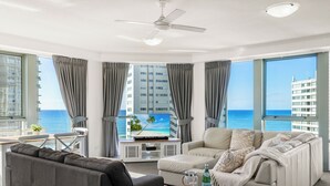 A modern living room with a sofa, armchair, and a TV displaying a beach scene. - Sun City Ocean Views (Surfers Paradise)