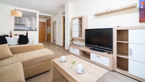 A modern living room with a sofa, a coffee table with cups and a flower, a TV, and a kitchen area in the background. - Beautiful and cheerful holiday house in Javea, Costa Blanca, Spain  with communal pool for 2 persons (Javea)