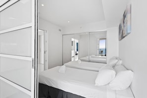 A modern hotel room with a large bed, a glass partition, and a view of the beach. - H Residences Ocean View (Surfers Paradise)