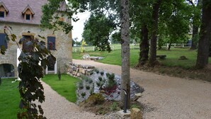 A stone building with a gravel path leading to a pond, surrounded by trees and a white fence.