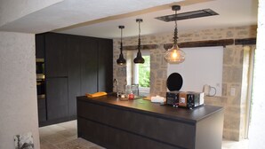 A modern kitchen with dark cabinetry, a central island, hanging pendant lights, and a stone wall.