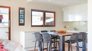 A compact kitchen with a dining area, featuring a wooden table, four chairs, a large window, and a sign above the window.