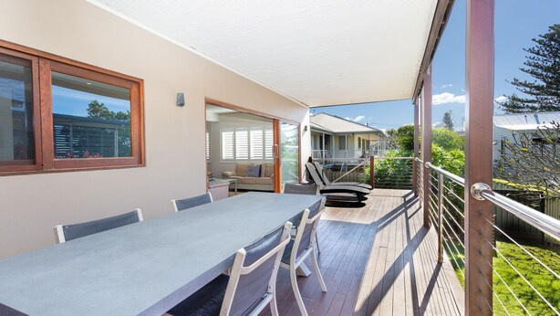 En balkon med bord og stole, en skydedør der fører til en opholdsstue, og udsigt til et nabohus.