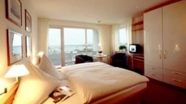 A hotel room with a bed, a desk, a TV, and a view of the sea.