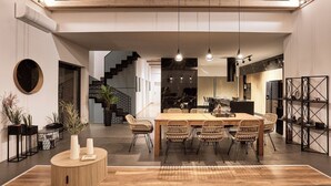 A spacious dining area with a high ceiling and exposed wooden beams, a modern kitchen with black cabinetry, and a staircase with a geometric design. - BBQ & Jacuzzi★HEATED pool★Big Garden★2 cars rental included★18 sleeps (Alikianos)