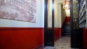 Un passadís amb una paret vermella i blanca, una porta gran amb marc negre i una escala que condueix a un pis superior.