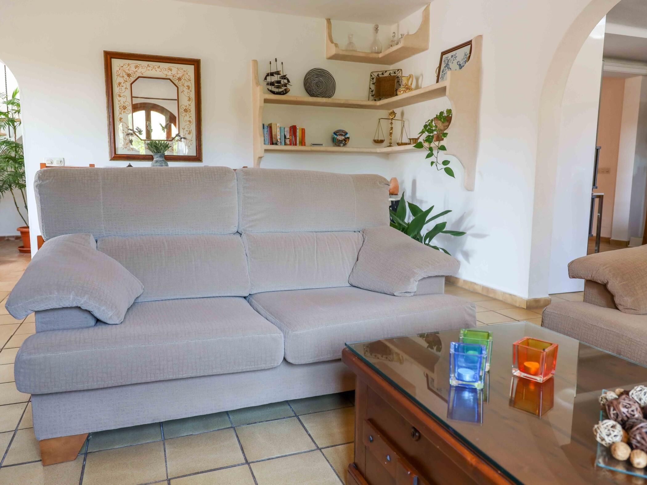 A living room with a sofa, a glass coffee table, and a bookshelf with decorative items.