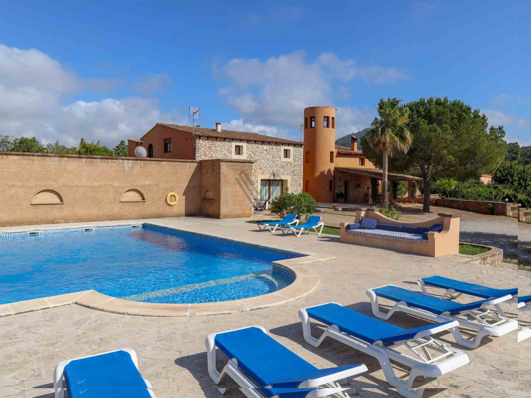 A pool area with lounge chairs, a stone building, and a tower.