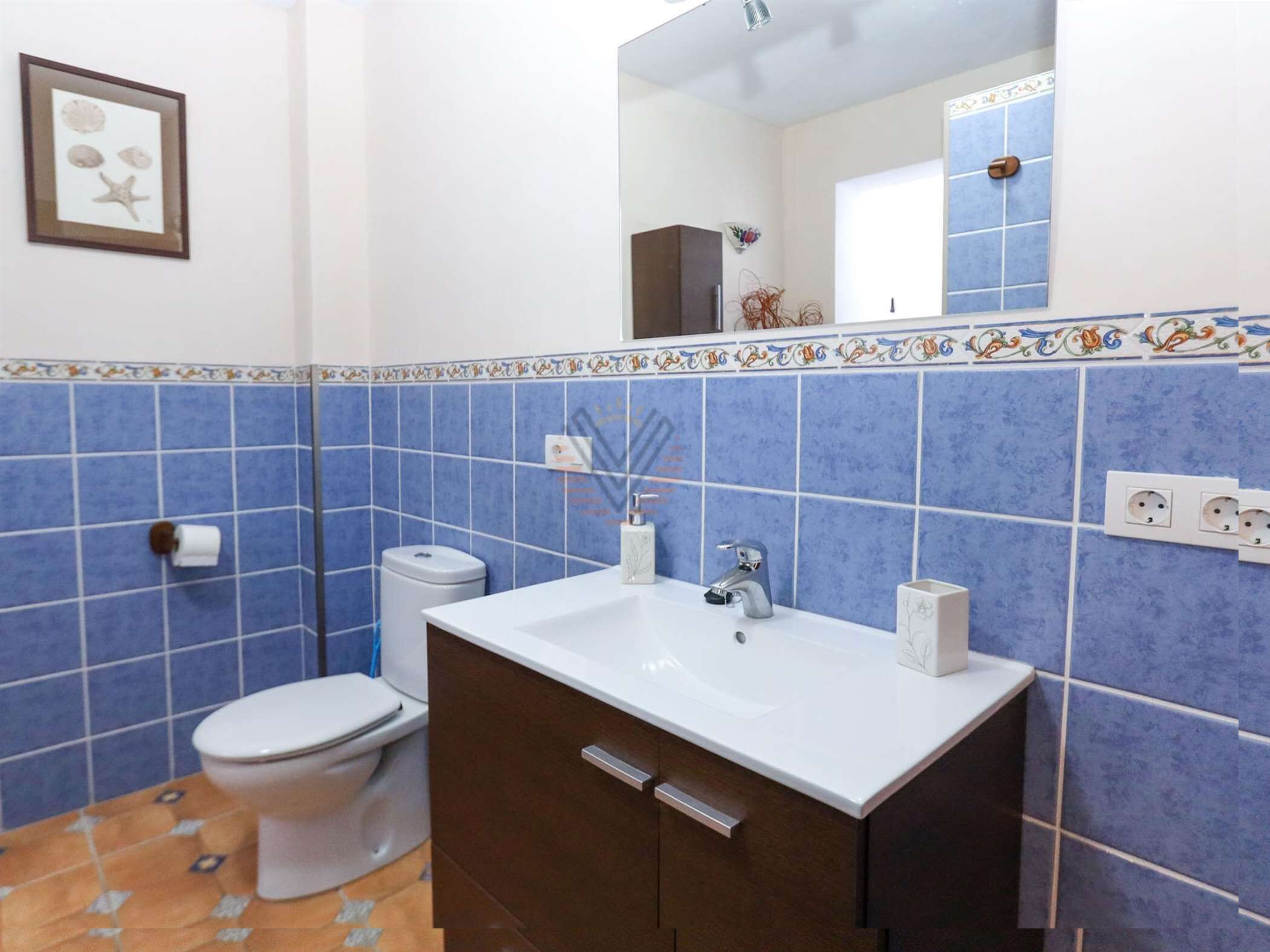 A bathroom with a white sink, dark brown cabinet, blue tiled walls, and a framed picture on the wall.