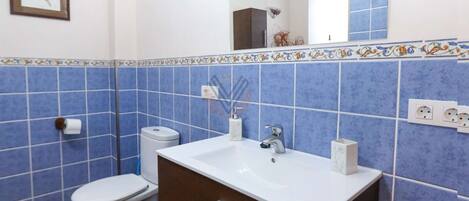 A bathroom with a white sink, dark brown cabinet, blue tiled walls, and a framed picture on the wall.