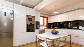 A modern kitchen with white cabinetry, a stainless steel refrigerator, a built-in oven, and a black microwave. There is a dining table with four chairs and a bowl of fruit on it. - Casa Fina, Holiday house in Felanitx, Mallorca (Felanitx)