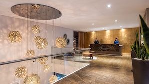 A modern hotel lobby with a reception desk, geometric patterned lighting, a glass railing, and a marble floor.