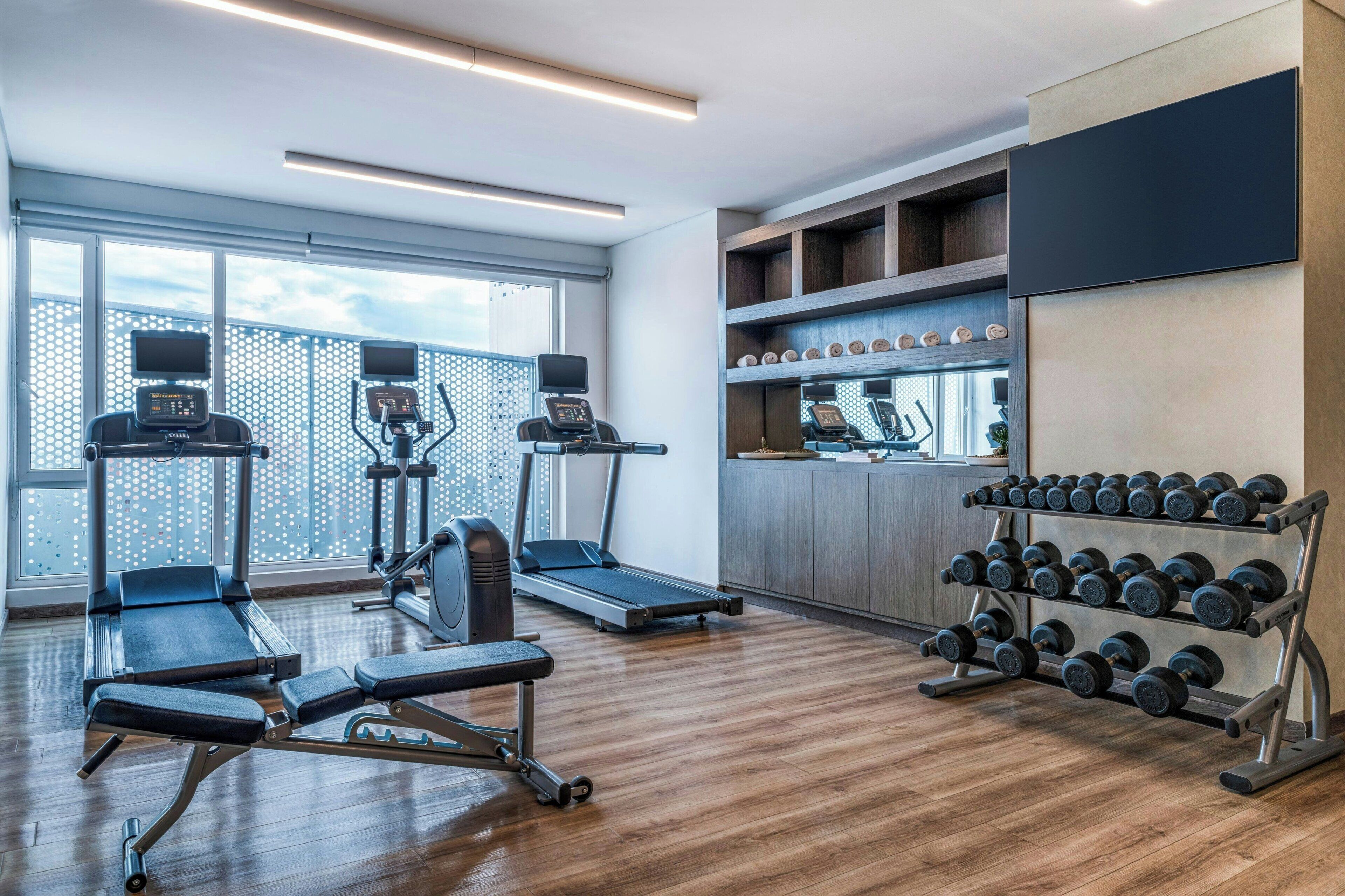 Een moderne sportschool met cardioapparaten, gewichten en een televisie aan de muur.