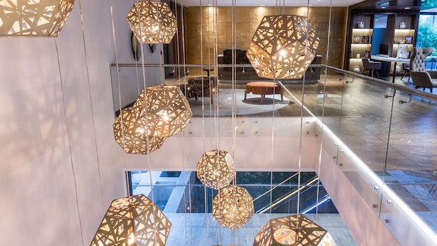A modern hotel lobby with geometric hanging lights, a seating area, and a staircase.