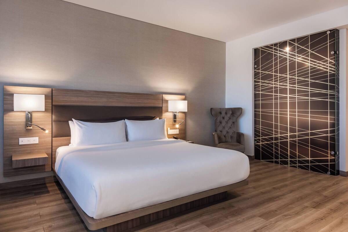 Una habitación de hotel moderna con una cama grande, dos lámparas de noche, un cabecero de madera y un papel tapiz con estampado geométrico.