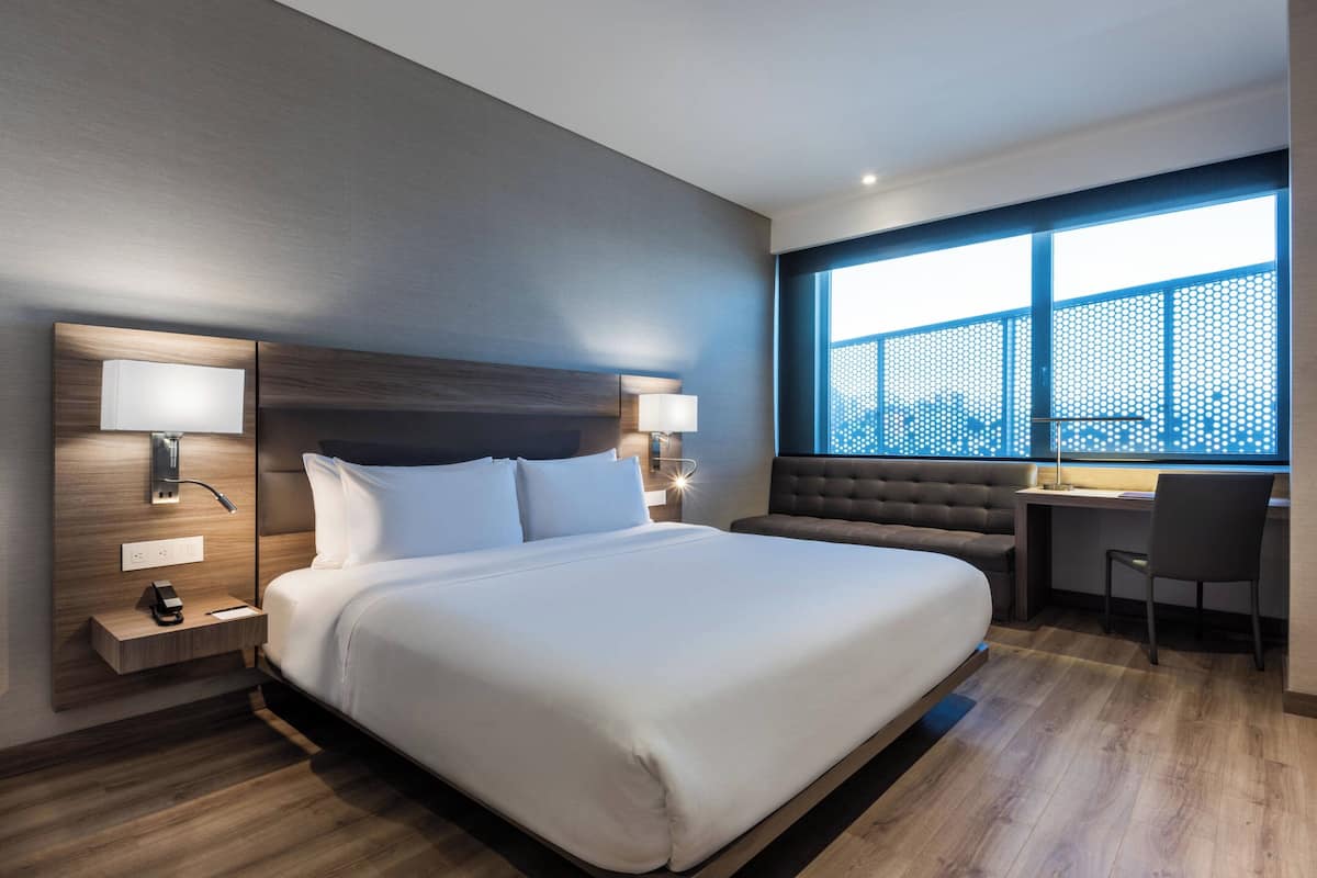 Habitación de hotel moderna con una cama grande, lámparas de noche, un escritorio y vistas a través de un ventanal amplio.