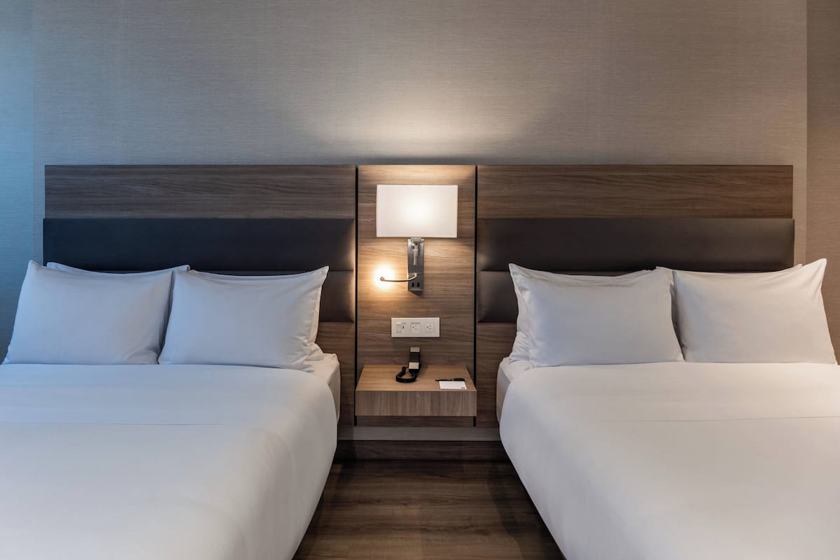 Habitación de hotel con dos camas, una mesita de noche con lámpara y una lámpara de pared.