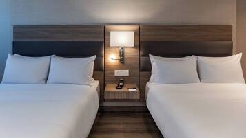 A hotel room with two beds, a nightstand with a lamp, and a wall-mounted light fixture.