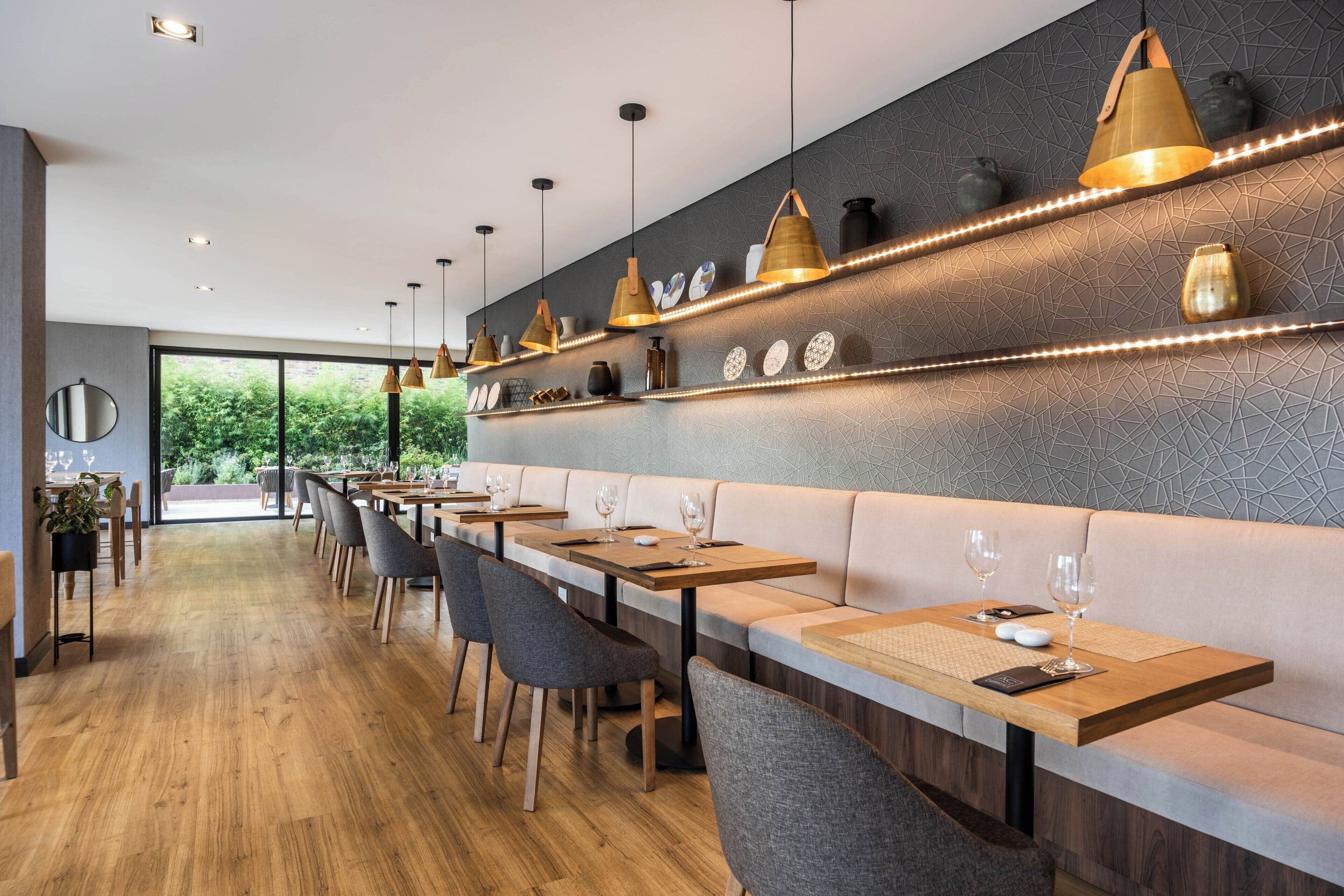 Un restaurant moderne avec des tables en bois, des sièges rembourrés, des luminaires suspendus et des vases décoratifs disposés sur des étagères.