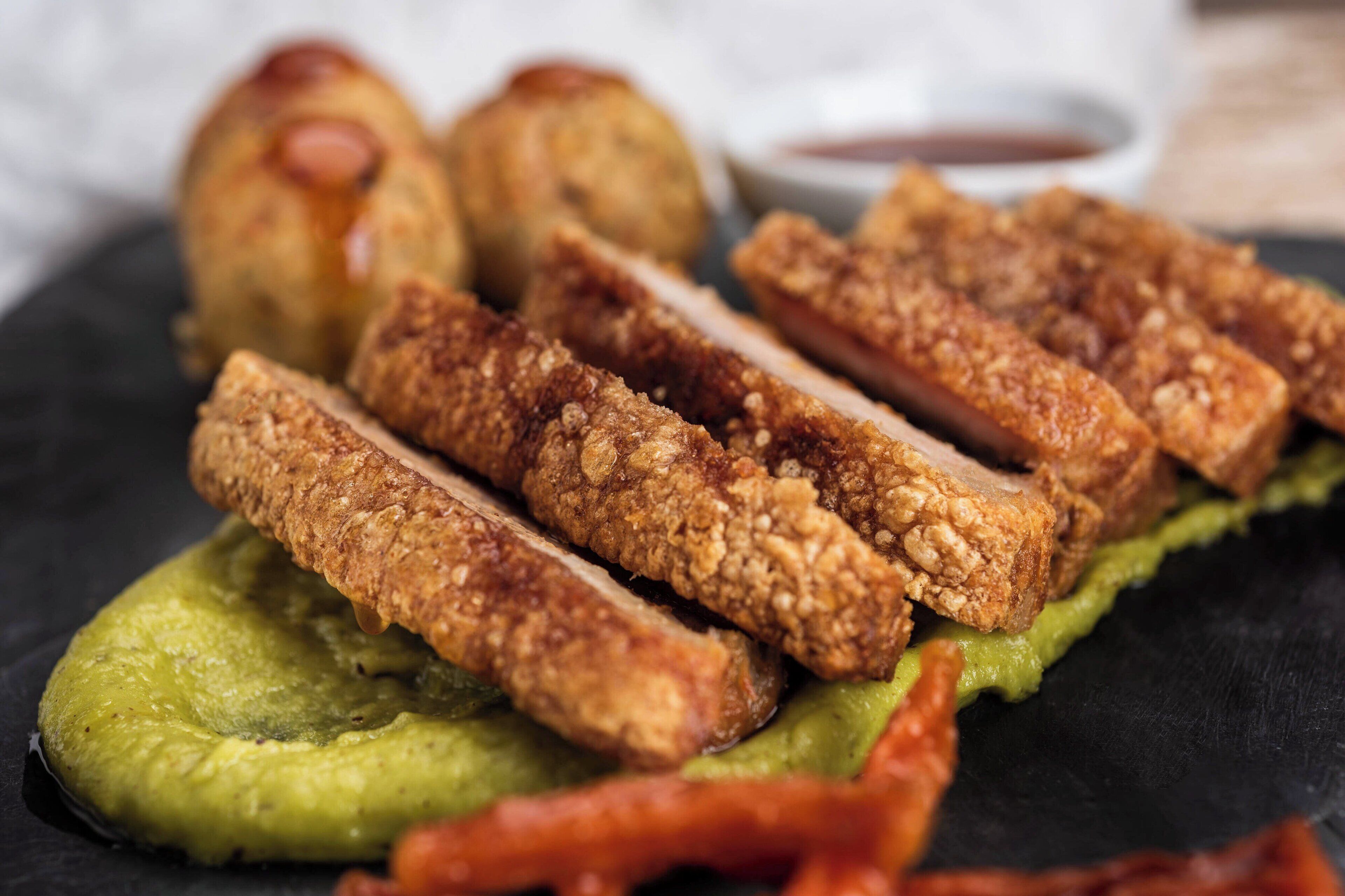 Een bord met gefrituurd vlees, een groene saus en een klein schaaltje saus.