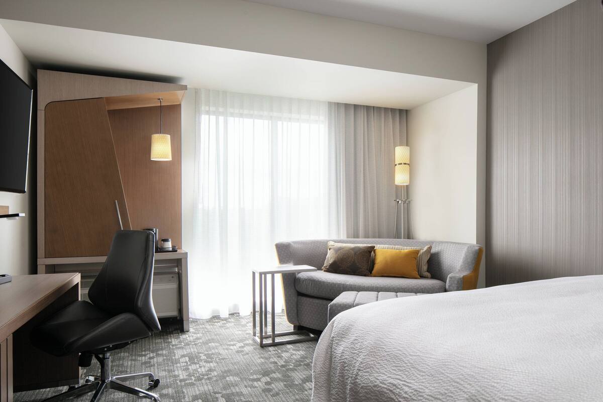 A hotel room with a desk, two chairs, a bed, and a TV.