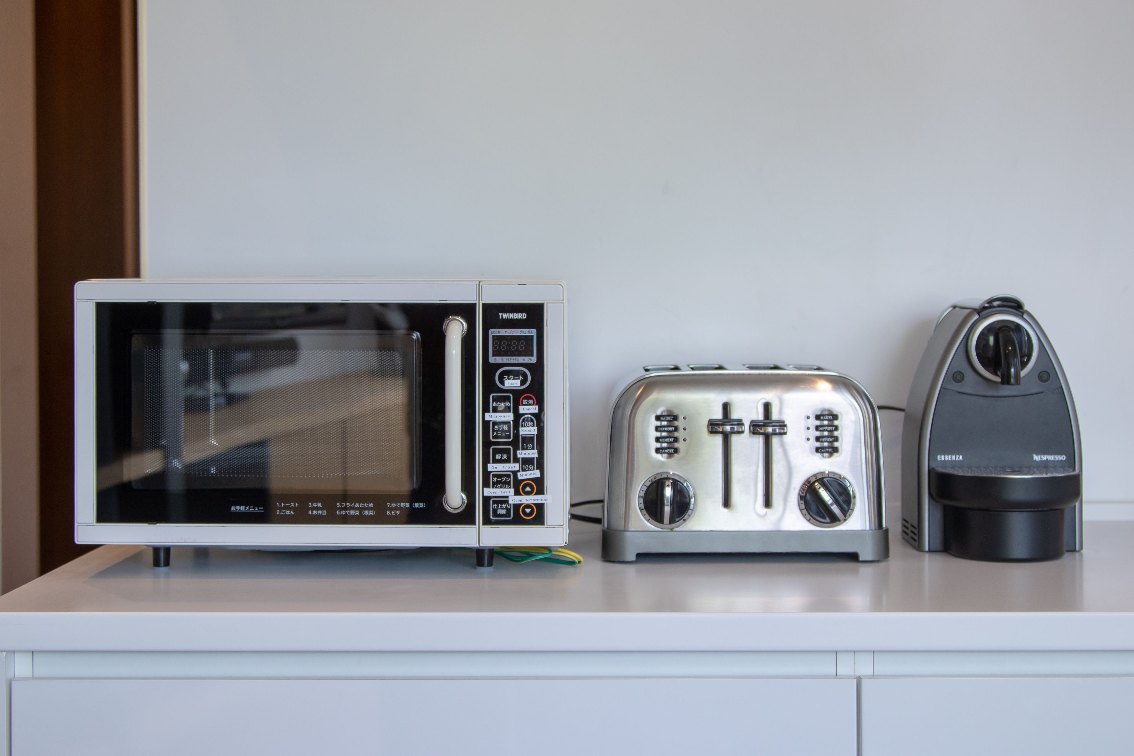 Una cocina con microondas, tostadora y máquina de espresso sobre una encimera blanca.