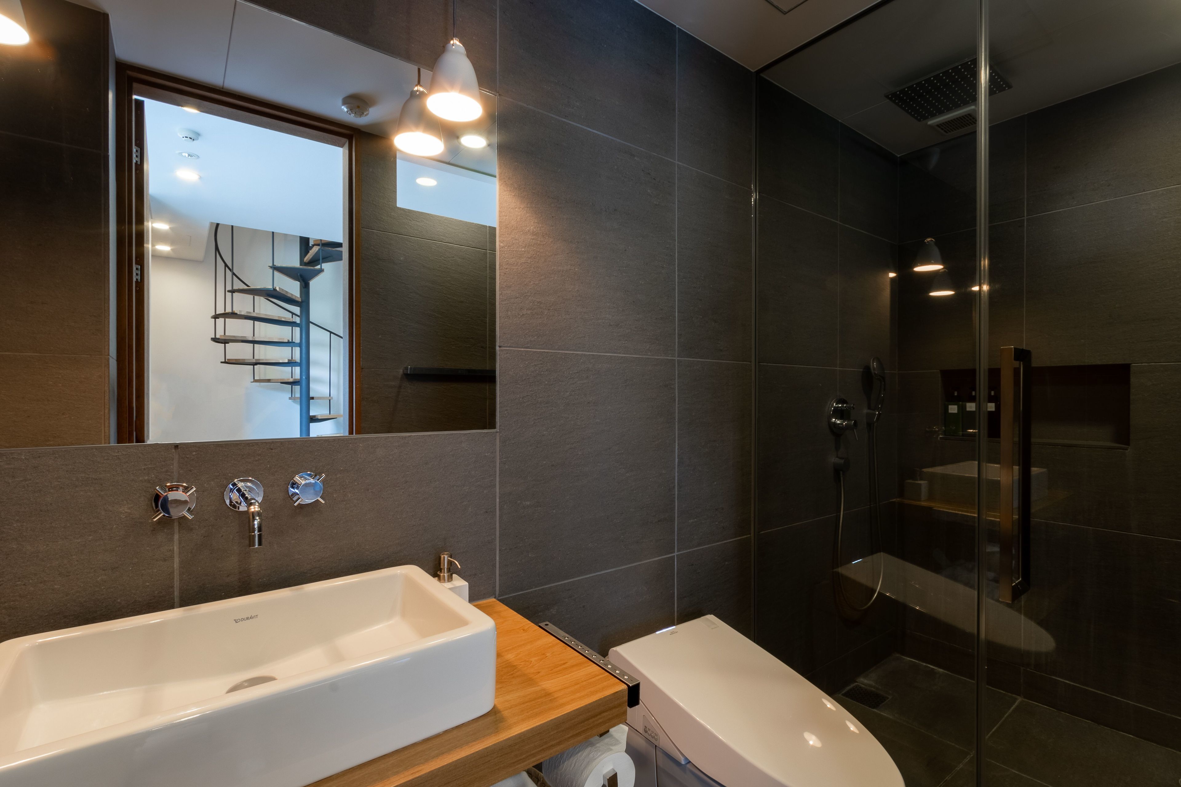 Un baño moderno con un lavamanos grande de color blanco, un espejo y una ducha con cerramiento de vidrio.